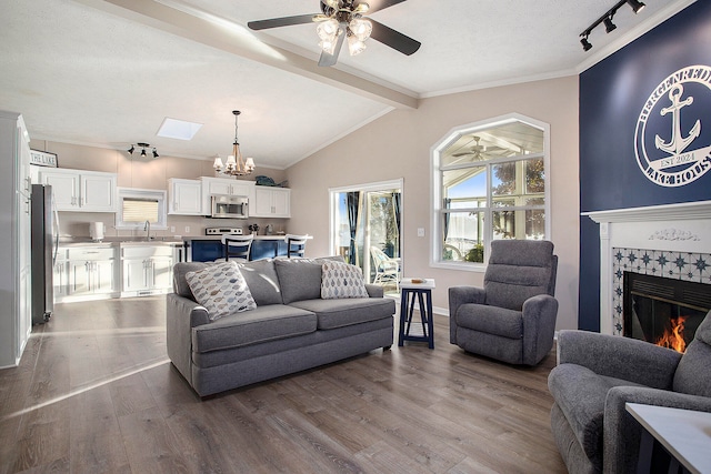 living room with ceiling fan with notable chandelier, light wood-type flooring, lofted ceiling with skylight, and a fireplace