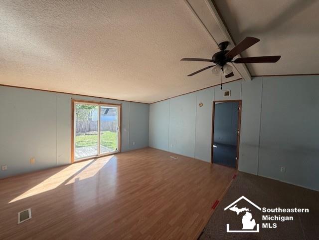 unfurnished living room with vaulted ceiling with beams, ceiling fan, wood-type flooring, and a textured ceiling