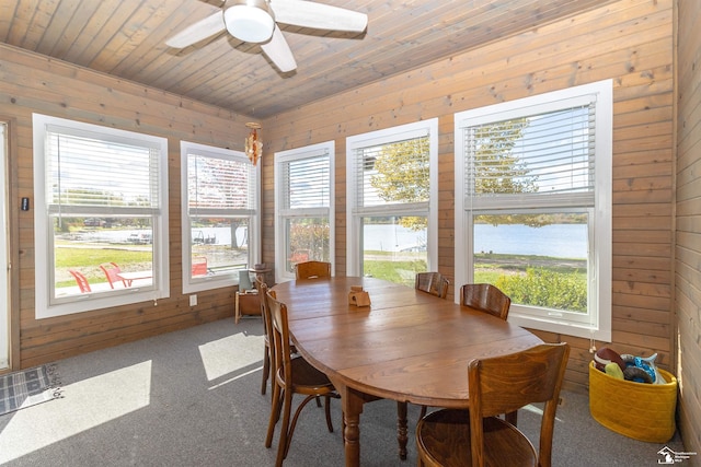 carpeted dining area featuring a water view, ceiling fan, wooden walls, and wood ceiling