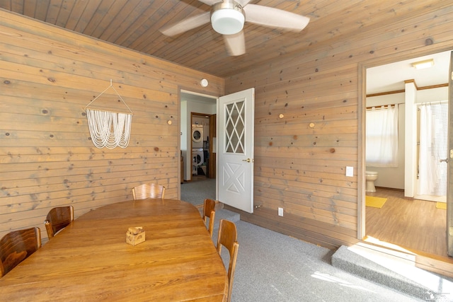 carpeted dining room featuring wooden walls, ceiling fan, wood ceiling, and stacked washer / drying machine