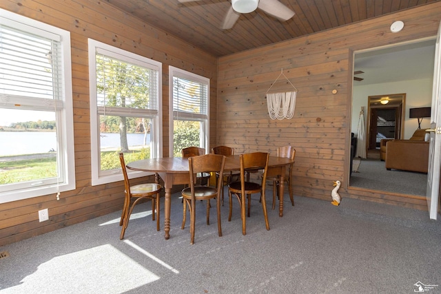 carpeted dining space with a water view, ceiling fan, wooden ceiling, and wood walls