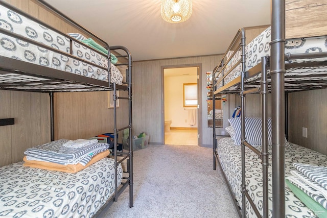 bedroom with wooden walls, light colored carpet, and ensuite bathroom