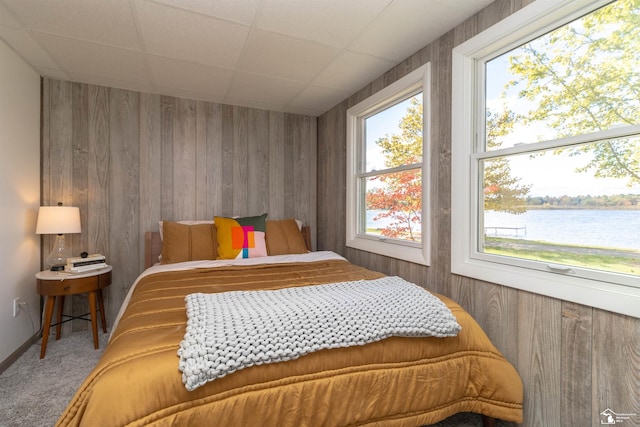 bedroom with carpet, multiple windows, wooden walls, and a water view