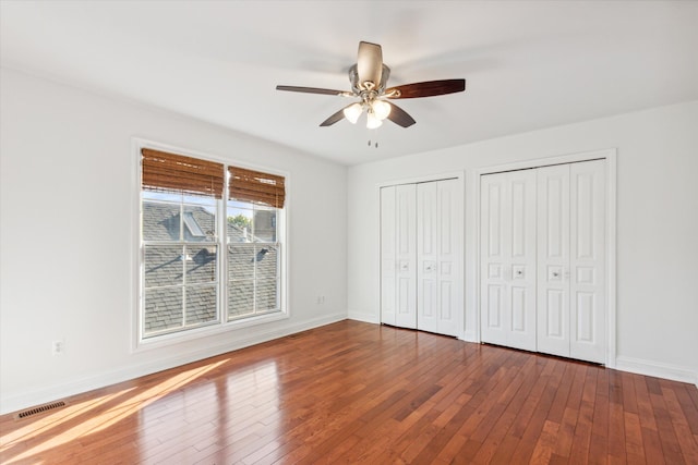 unfurnished bedroom with hardwood / wood-style floors, ceiling fan, and multiple closets