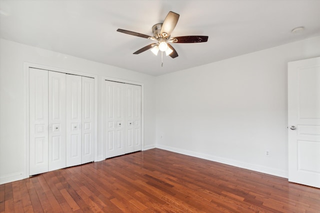 unfurnished bedroom with ceiling fan, dark hardwood / wood-style flooring, and two closets