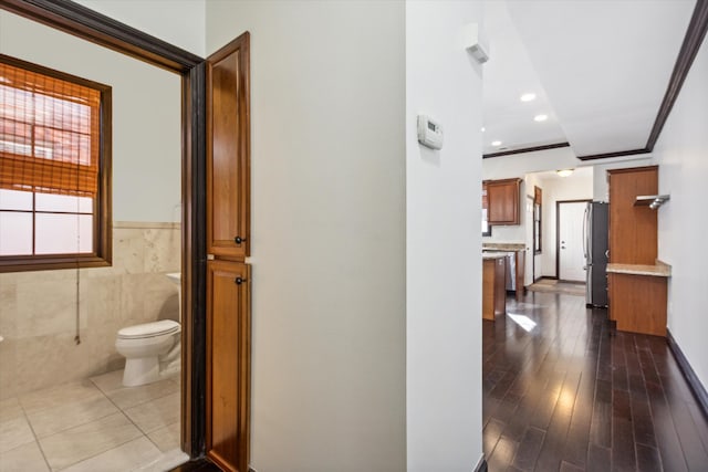 hallway featuring crown molding, dark hardwood / wood-style flooring, and tile walls