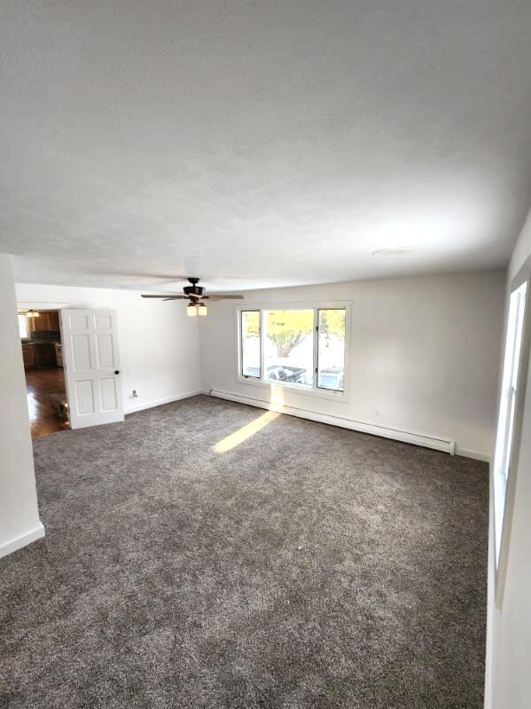 unfurnished living room with ceiling fan and dark colored carpet