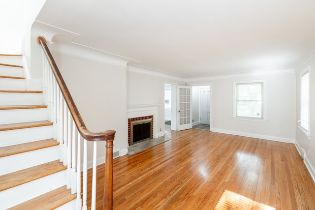 unfurnished living room featuring a brick fireplace, crown molding, and light wood-type flooring