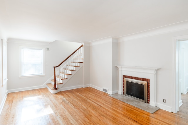 unfurnished living room with light hardwood / wood-style floors, a brick fireplace, and ornamental molding