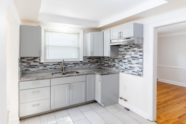 kitchen featuring backsplash, light stone counters, sink, and light hardwood / wood-style flooring