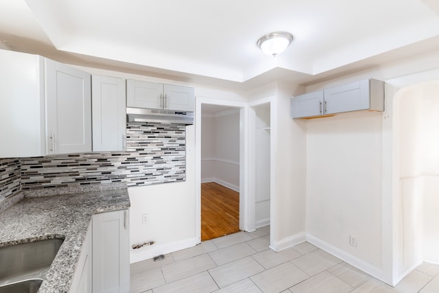 kitchen featuring light stone countertops, sink, light hardwood / wood-style flooring, a tray ceiling, and decorative backsplash