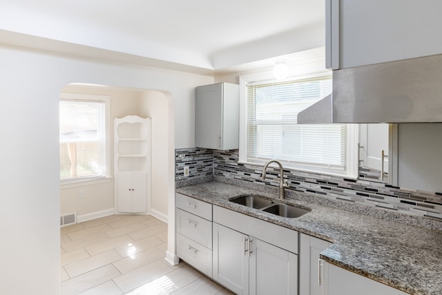 kitchen featuring light tile patterned flooring, backsplash, stone countertops, and sink