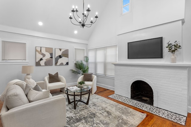 living room featuring an inviting chandelier, wood-type flooring, high vaulted ceiling, and a brick fireplace