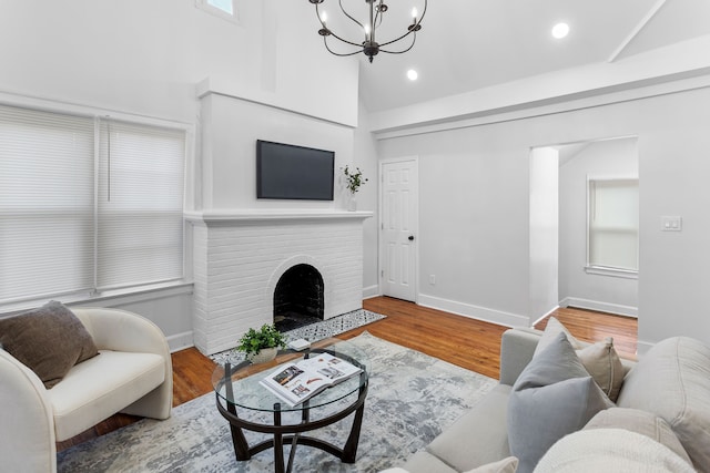 living room with hardwood / wood-style floors, a notable chandelier, a healthy amount of sunlight, and a brick fireplace