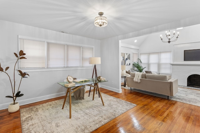 office featuring hardwood / wood-style flooring, a fireplace, lofted ceiling, and a notable chandelier