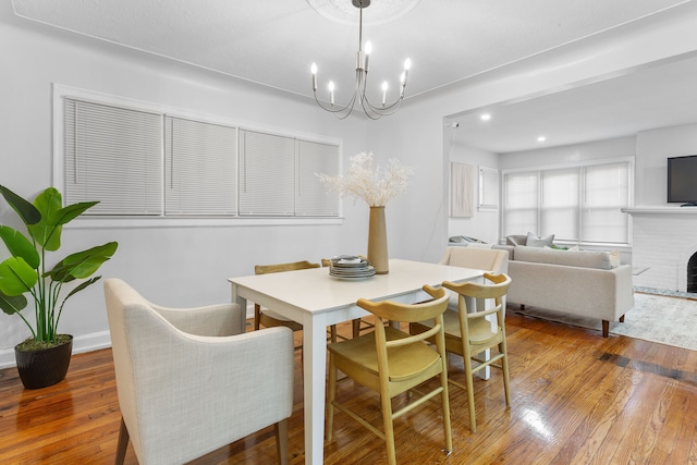 dining space featuring an inviting chandelier, hardwood / wood-style flooring, and a brick fireplace