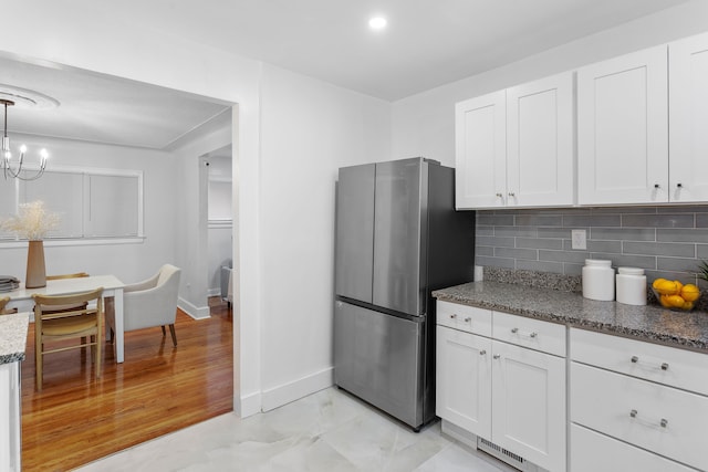 kitchen featuring pendant lighting, backsplash, dark stone countertops, white cabinetry, and stainless steel refrigerator