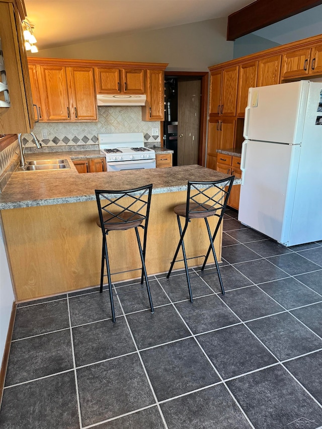 kitchen with white appliances, sink, vaulted ceiling with beams, dark tile patterned floors, and a breakfast bar area