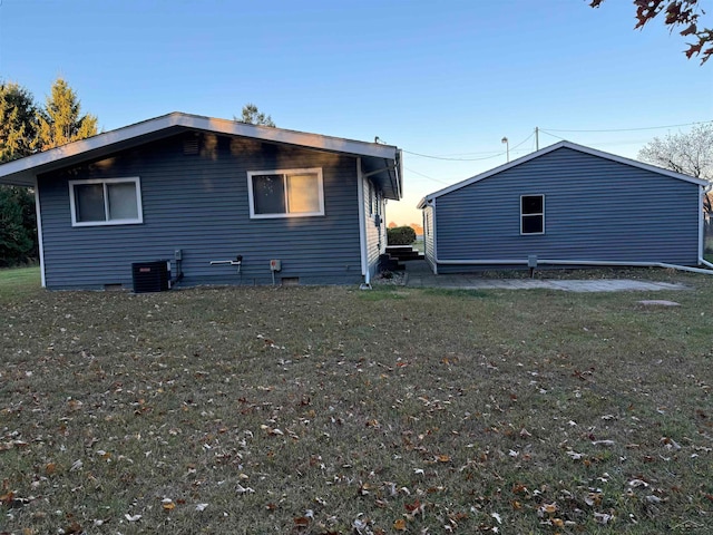 back house at dusk with a yard and central AC unit