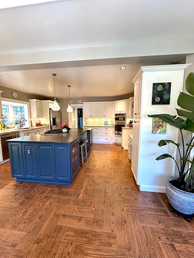 kitchen featuring white cabinetry, blue cabinets, a spacious island, decorative light fixtures, and appliances with stainless steel finishes