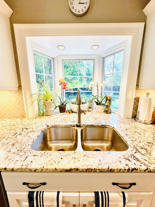 room details featuring light stone countertops, white cabinetry, and sink