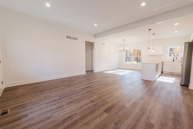 unfurnished living room with a notable chandelier, dark hardwood / wood-style flooring, sink, and vaulted ceiling