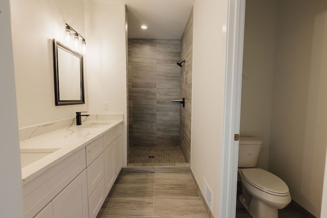 bathroom featuring a tile shower, tile patterned flooring, vanity, and toilet