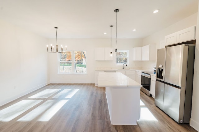 kitchen with stainless steel appliances, a kitchen island, decorative light fixtures, white cabinets, and light wood-type flooring