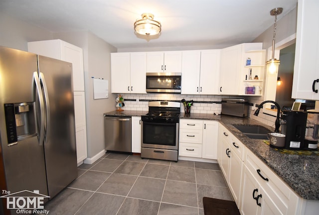 kitchen featuring appliances with stainless steel finishes, dark stone counters, sink, white cabinetry, and hanging light fixtures