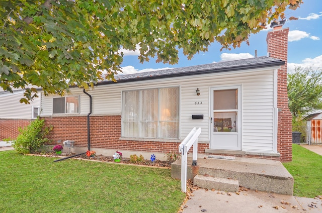 bungalow with entry steps, brick siding, a chimney, and a front lawn