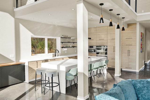 kitchen featuring sink, light brown cabinets, a high ceiling, pendant lighting, and a breakfast bar