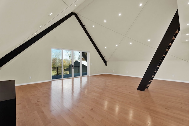 unfurnished living room with beam ceiling, high vaulted ceiling, and light wood-type flooring