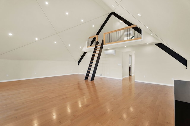 unfurnished living room with light wood-type flooring, high vaulted ceiling, and an AC wall unit