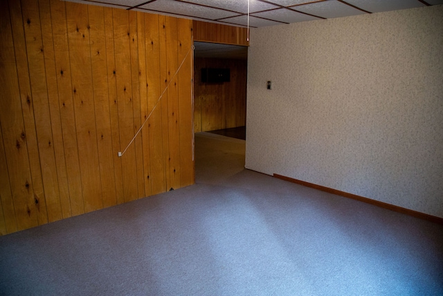 basement with a drop ceiling and wood walls