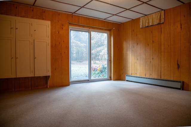 carpeted spare room featuring baseboard heating, wooden walls, and a drop ceiling