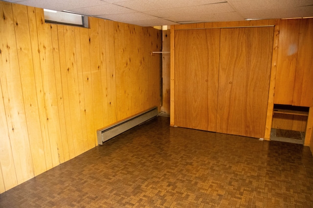 basement with dark parquet floors, a drop ceiling, a baseboard heating unit, and wood walls