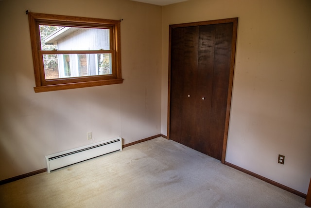 unfurnished bedroom with a closet, baseboard heating, and light colored carpet