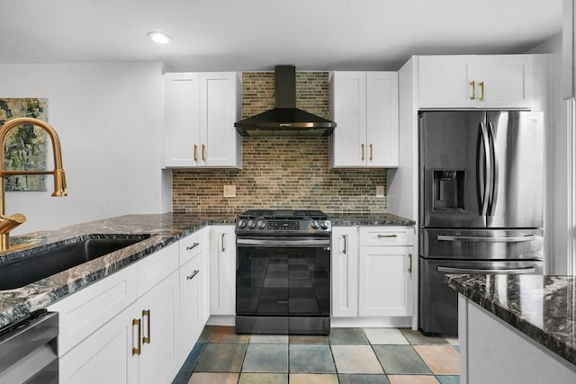 kitchen featuring appliances with stainless steel finishes, dark stone counters, sink, wall chimney range hood, and white cabinets