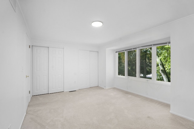 unfurnished bedroom featuring multiple closets, light carpet, and crown molding