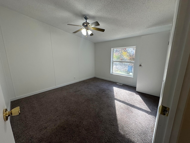 empty room with a textured ceiling, dark carpet, and ceiling fan