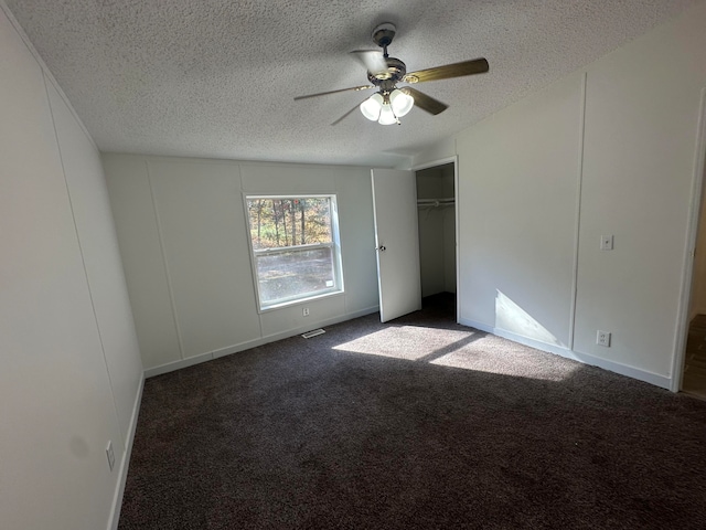 unfurnished bedroom featuring ceiling fan, dark carpet, and a textured ceiling