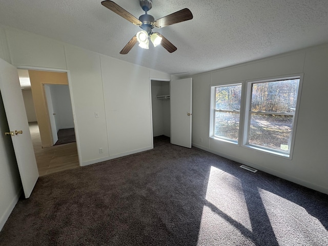 unfurnished bedroom featuring dark colored carpet, ceiling fan, a textured ceiling, and a closet