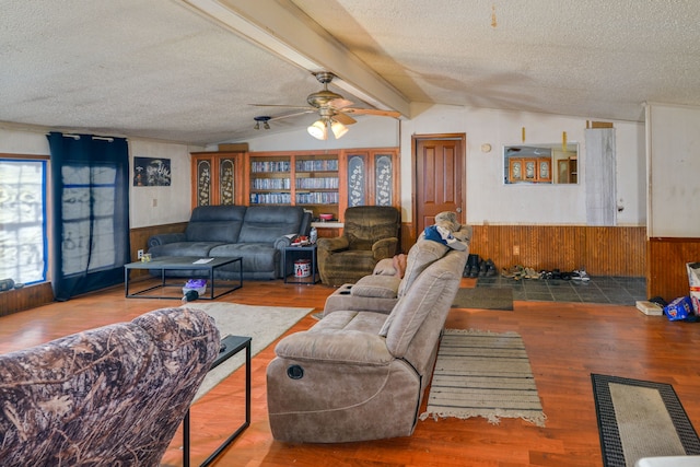 living room with wood walls, lofted ceiling with beams, hardwood / wood-style flooring, ceiling fan, and a textured ceiling