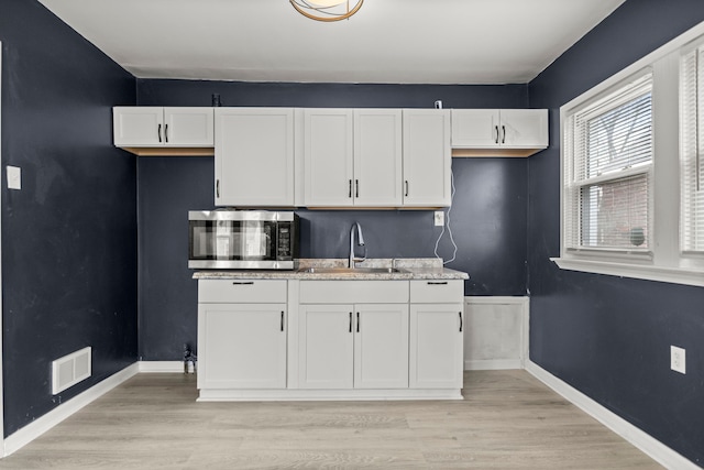 kitchen with white cabinets, light stone counters, light hardwood / wood-style flooring, and sink