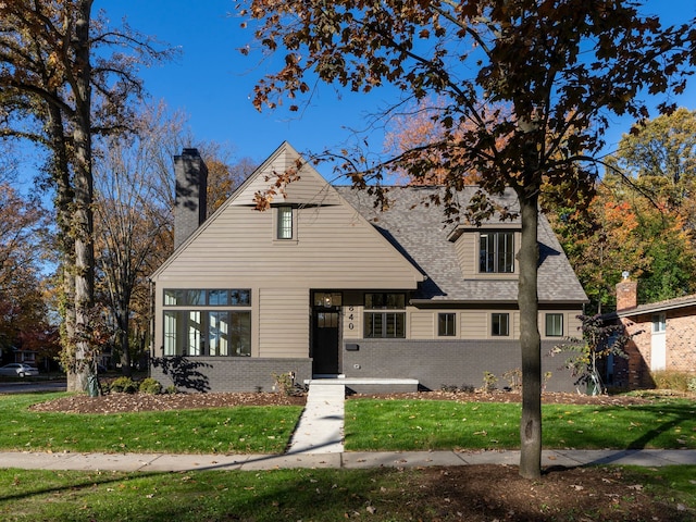 view of front of property featuring brick siding, a chimney, a shingled roof, and a front lawn