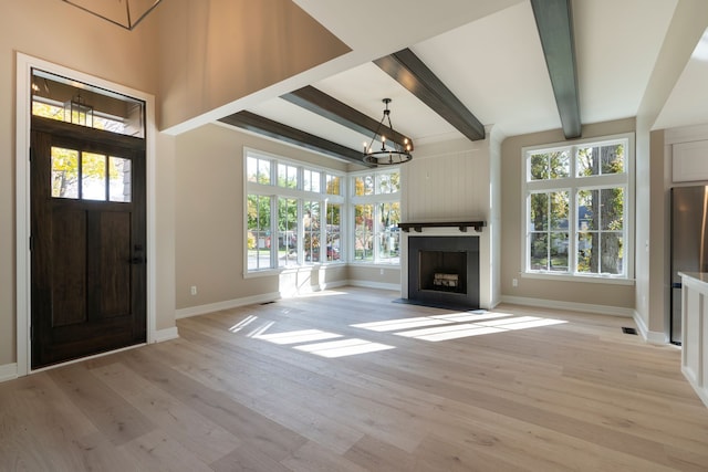 entrance foyer featuring baseboards, beam ceiling, a fireplace with flush hearth, light wood-style floors, and a notable chandelier