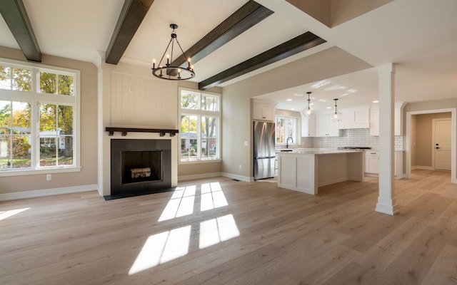 unfurnished living room featuring a wealth of natural light, beam ceiling, a large fireplace, and ornate columns