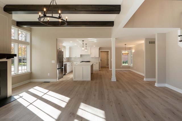 unfurnished living room with beam ceiling, a notable chandelier, a healthy amount of sunlight, and visible vents