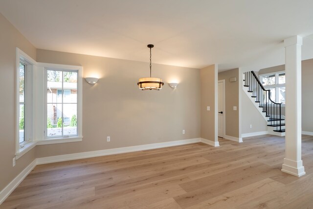 unfurnished dining area with stairway, light wood finished floors, baseboards, and decorative columns