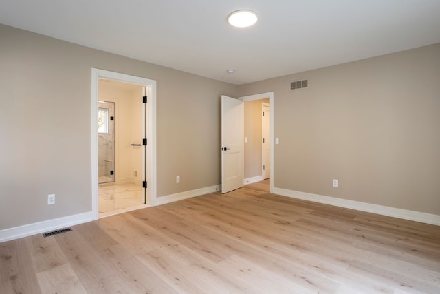 unfurnished bedroom with ensuite bath, baseboards, visible vents, and light wood-type flooring